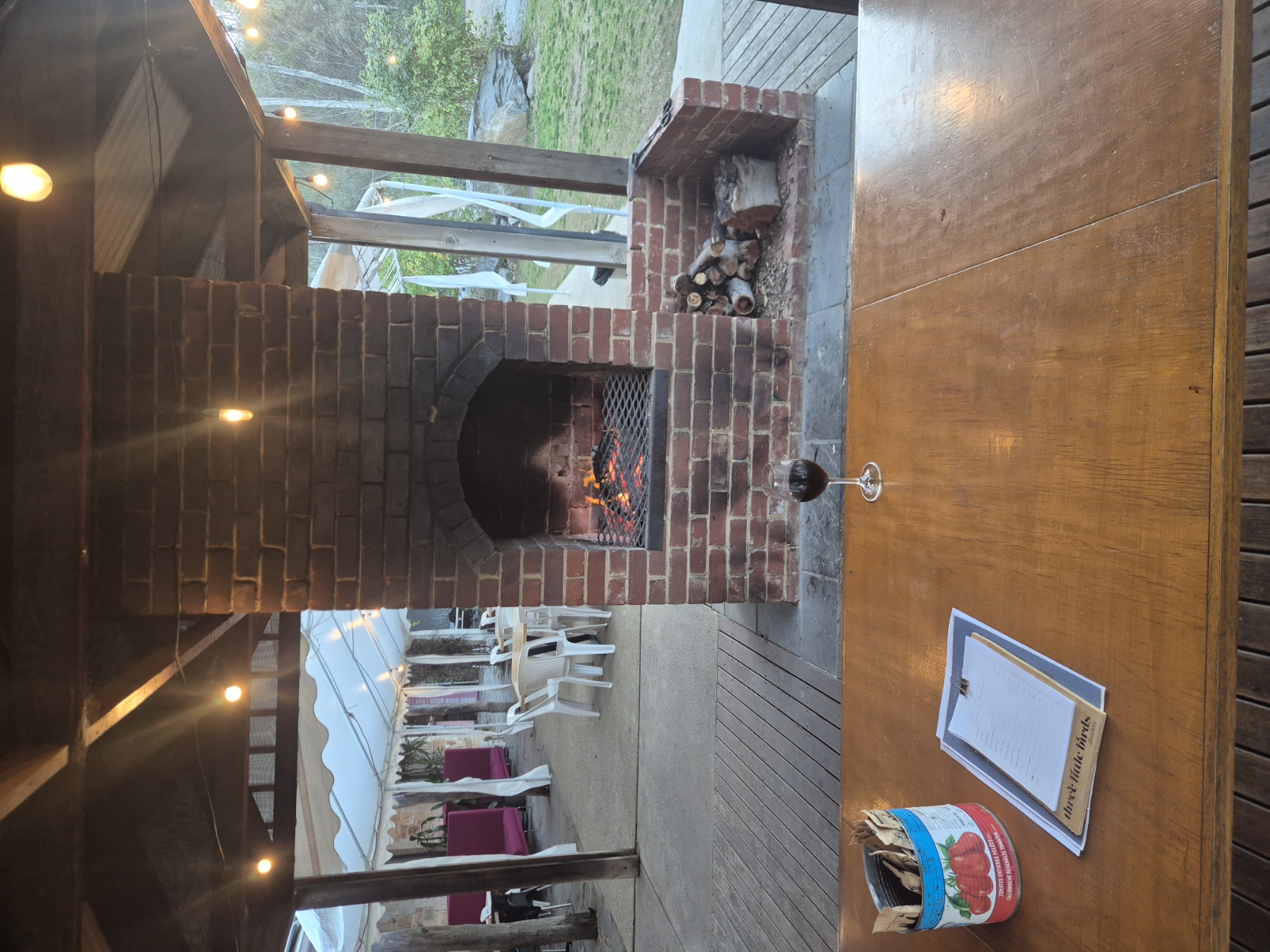 Open brick fireplace on the covered deck with a glass of red wine on the table