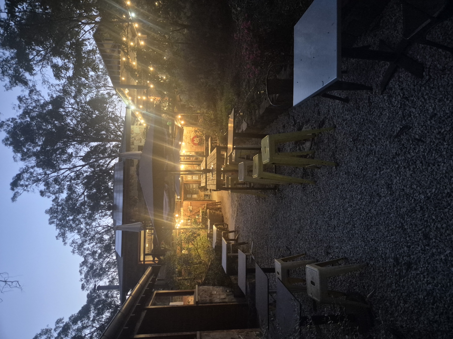 Festoon-lit gravel courtyard and tables outside the Three Little Birds Distillery at dusk